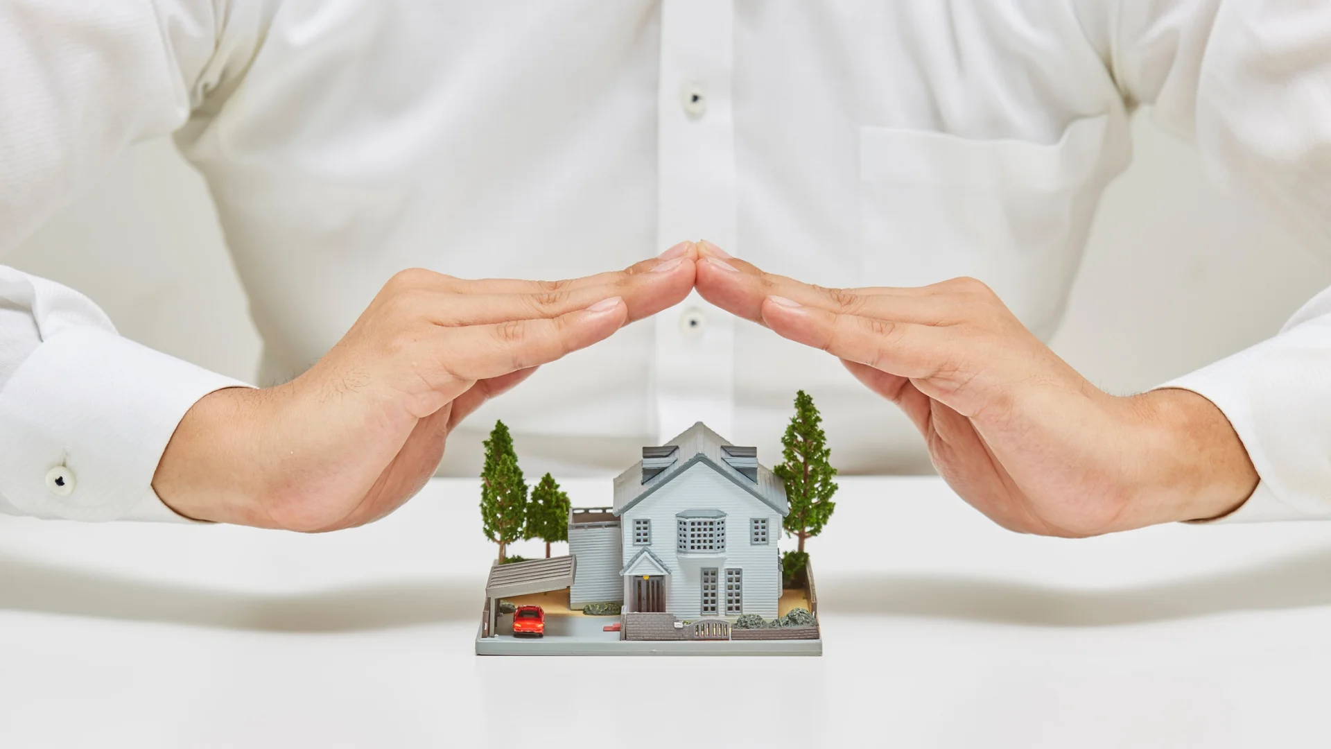 Hands protecting a small home model, representing safe home care support